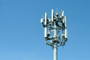 Cell tower with multiple antennas and equipment against a clear blue sky.
