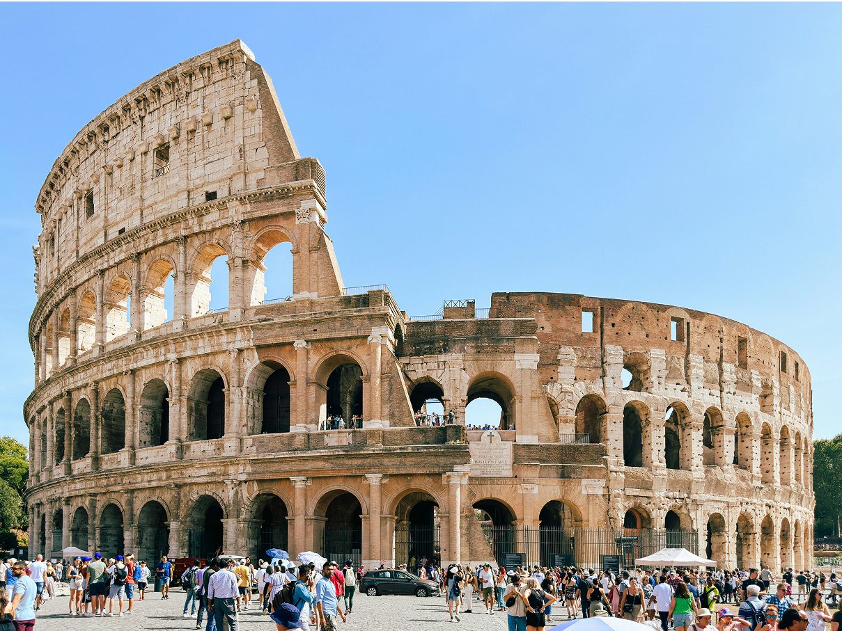 The Colosseum in Rome with crowds of tourists gathered outside on a sunny day