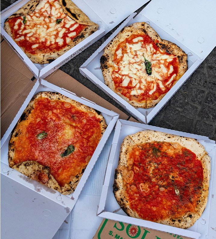 Four Neapolitan-style pizzas in open cardboard boxes with tomato sauce and cheese