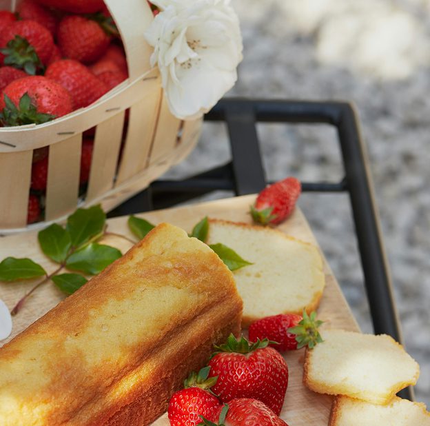 Loaf of pound cake with slices and fresh strawberries on a wooden board next to a basket of strawberries