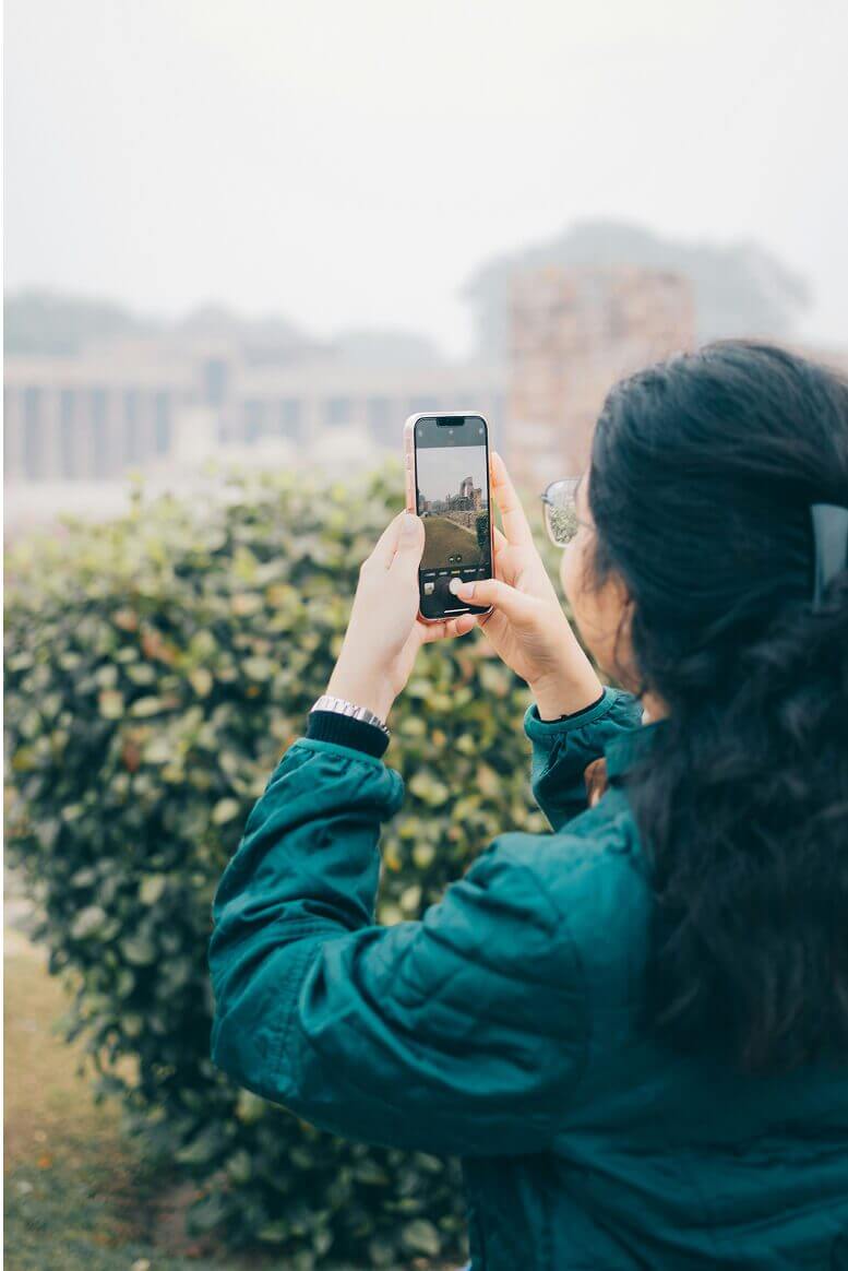 Person in a green jacket taking a photo of outdoor scenery with a smartphone
