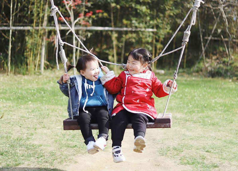 Two young children laughing and playing together on a swing outdoors